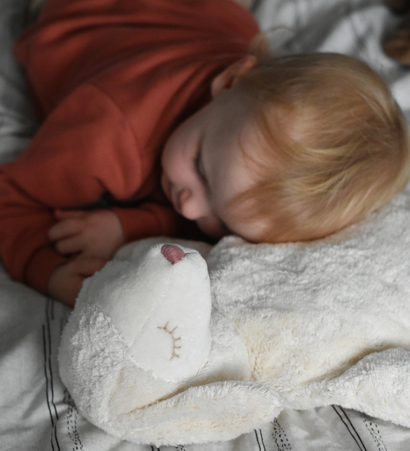 A young child laying down with his head resting on a Senger large white sheep cuddly soft toy. This cuddly sheep is made with organic cotton and natural fillings. This sheep is part of a wide range of soft toys stocked at Babipur. 