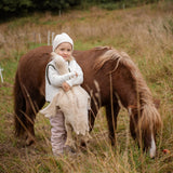 Child hugging a large cream Senger cuddly goose in a grassy field standing next to a horse. 