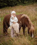 Child hugging a large cream Senger cuddly goose in a grassy field standing next to a horse. 