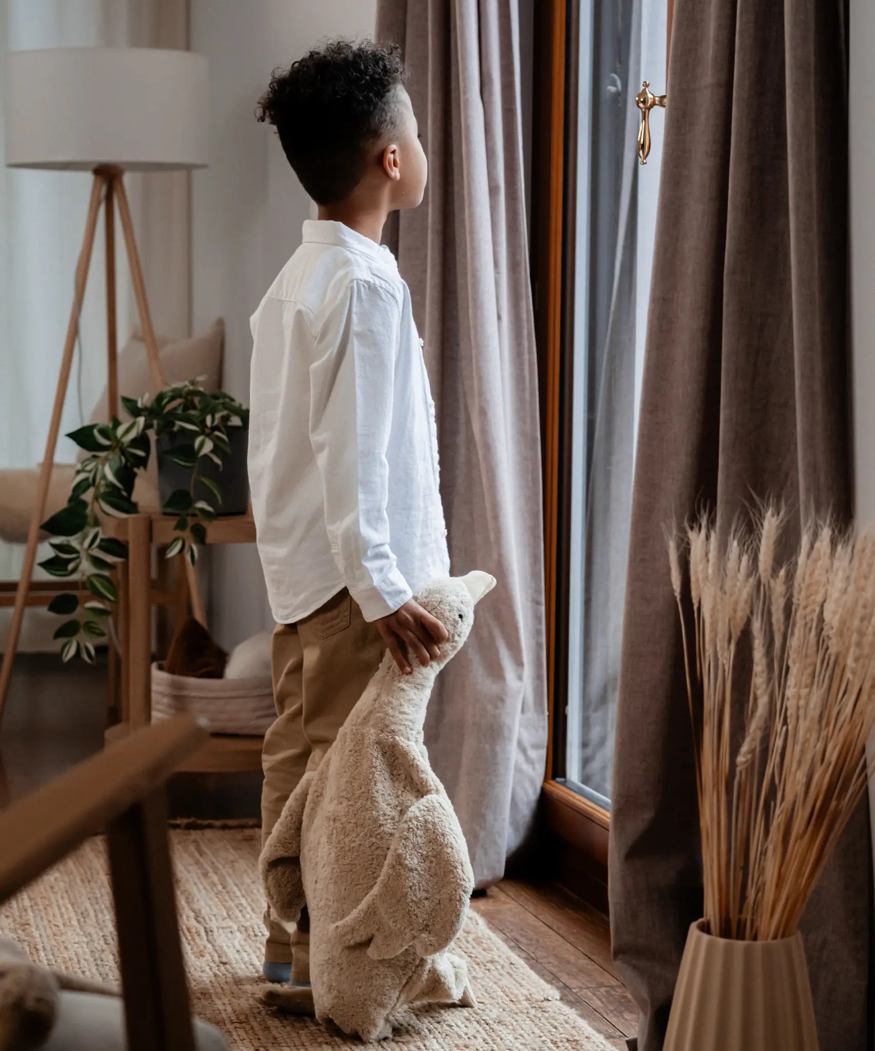 Child standing next to a large cream Senger cuddly goose soft toy and holding it's head in a living room 