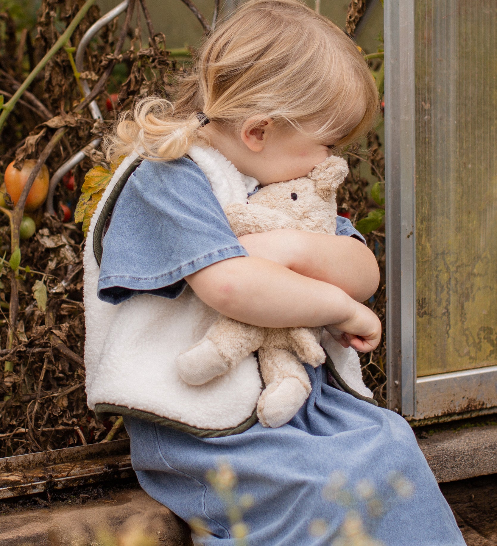 Child cuddling the Senger Naturwelt Small Cuddly Bear in Linen, organic heatable bear with removable cherry stone cushion.