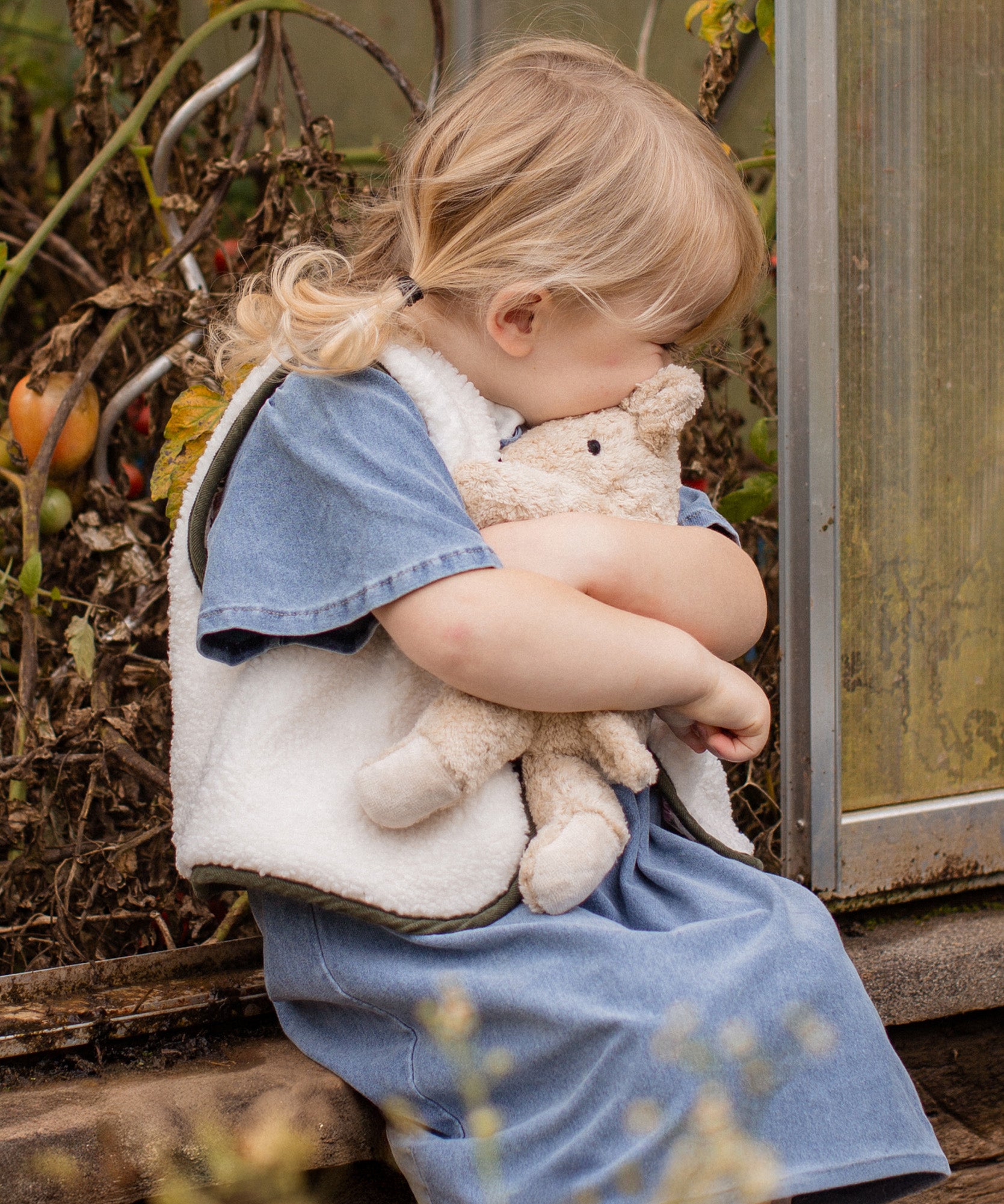 Child cuddling the Senger Naturwelt Small Cuddly Bear in Linen, organic heatable bear with removable cherry stone cushion.