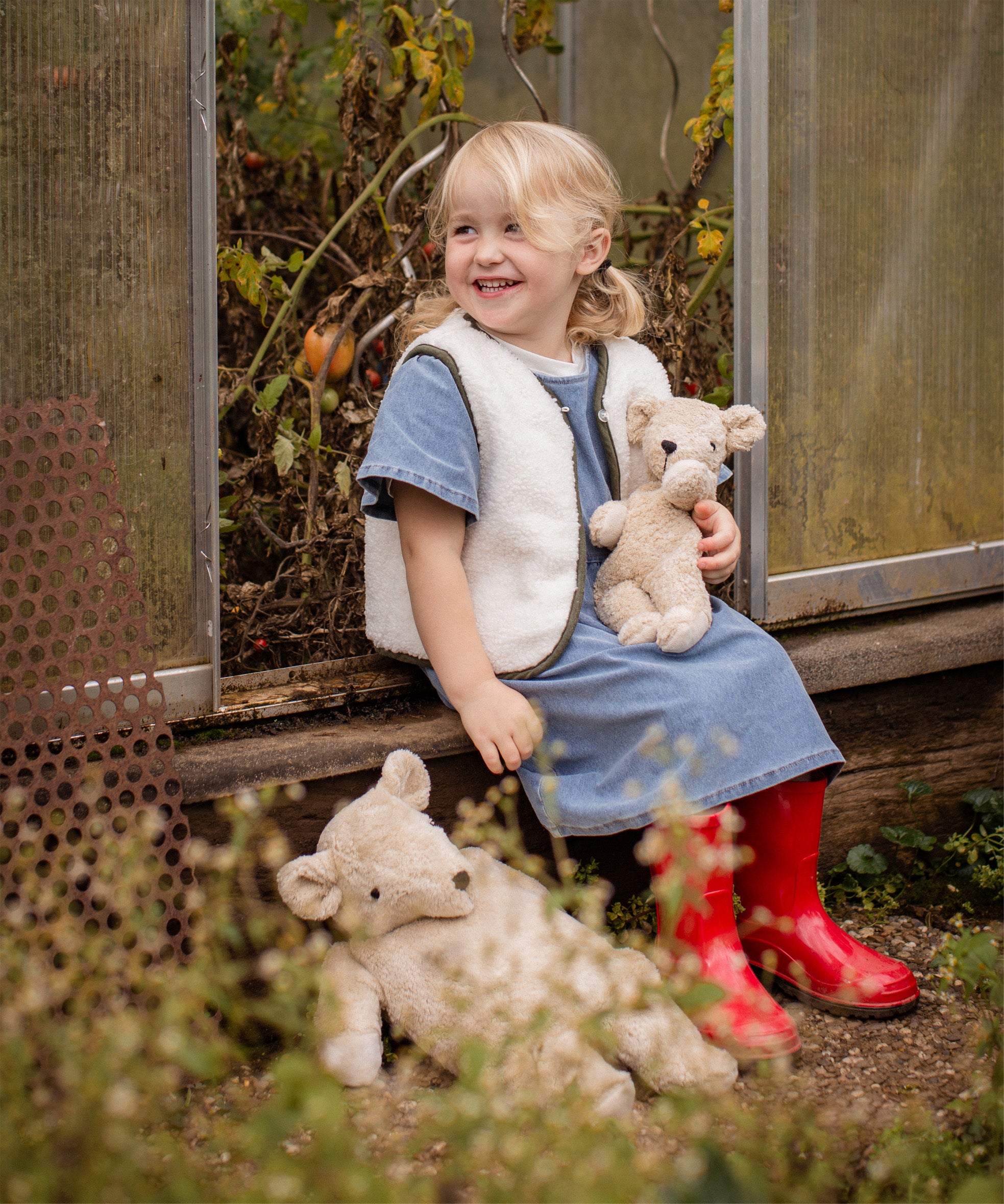 Child smiling while holding the Senger Naturwelt Small Cuddly Bear in Linen beside the larger Linen bear, organic heatable soft toys.