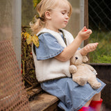 Child sitting outdoors holding the Senger Naturwelt Small Cuddly Bear in Linen, organic GOTS cotton heatable soft toy.