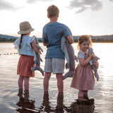 Children standing in shallow water holding the Senger Naturwelt Cuddly Shark, organic GOTS cotton heatable soft toy.
