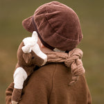 The back of a toddler carrying a Senger cuddly organic cotton cow soft toy over their shoulder