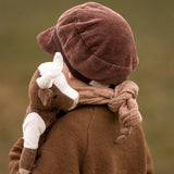 The back of a toddler carrying a Senger cuddly organic cotton cow soft toy over their shoulder