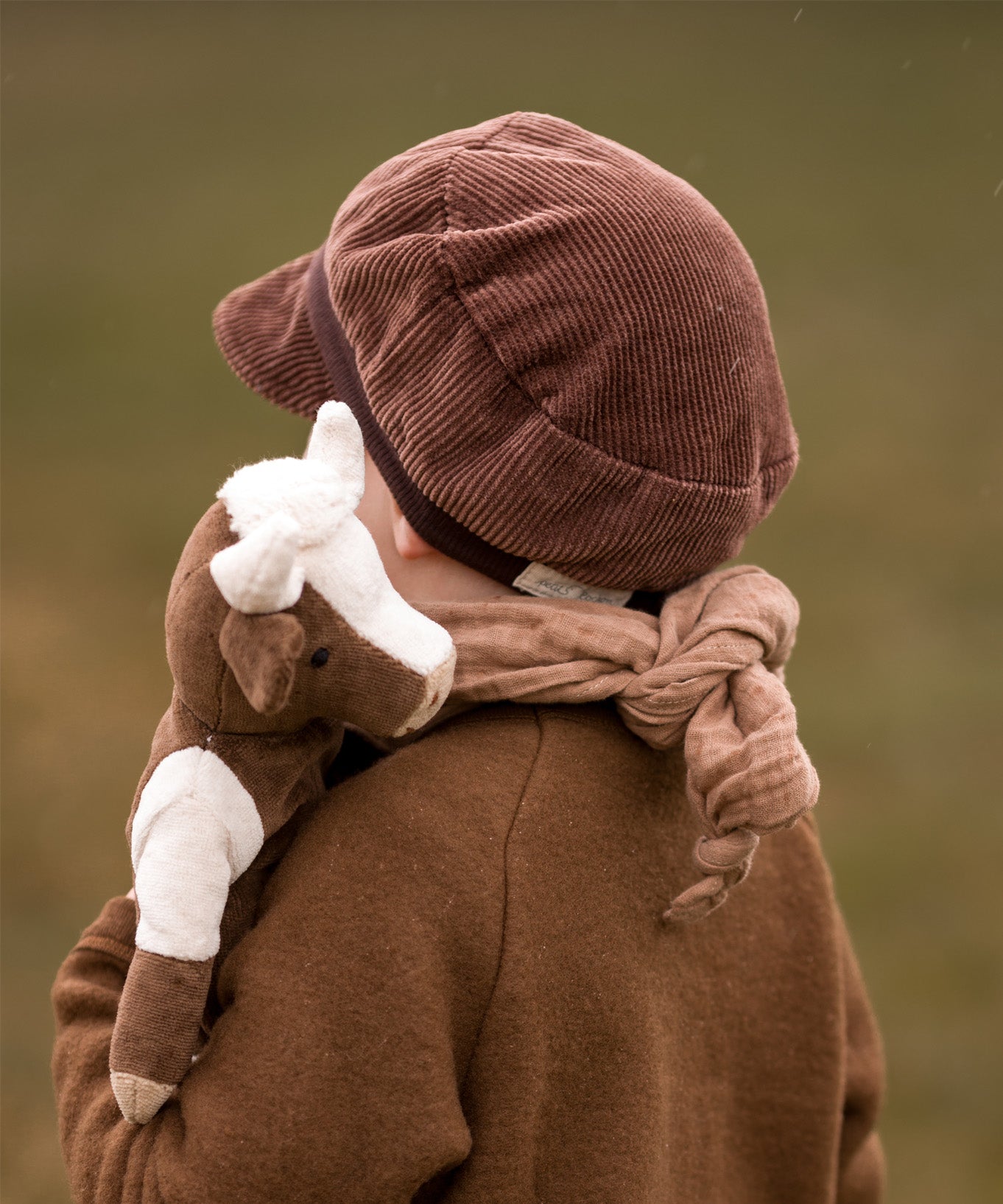 The back of a toddler carrying a Senger cuddly organic cotton cow soft toy over their shoulder