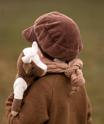 The back of a toddler carrying a Senger cuddly organic cotton cow soft toy over their shoulder