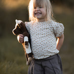 A little girls in a field, holding the Senger organic cotton floppy cow stuffed animal toy. 