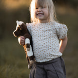 A little girls in a field, holding the Senger organic cotton floppy cow stuffed animal toy. 