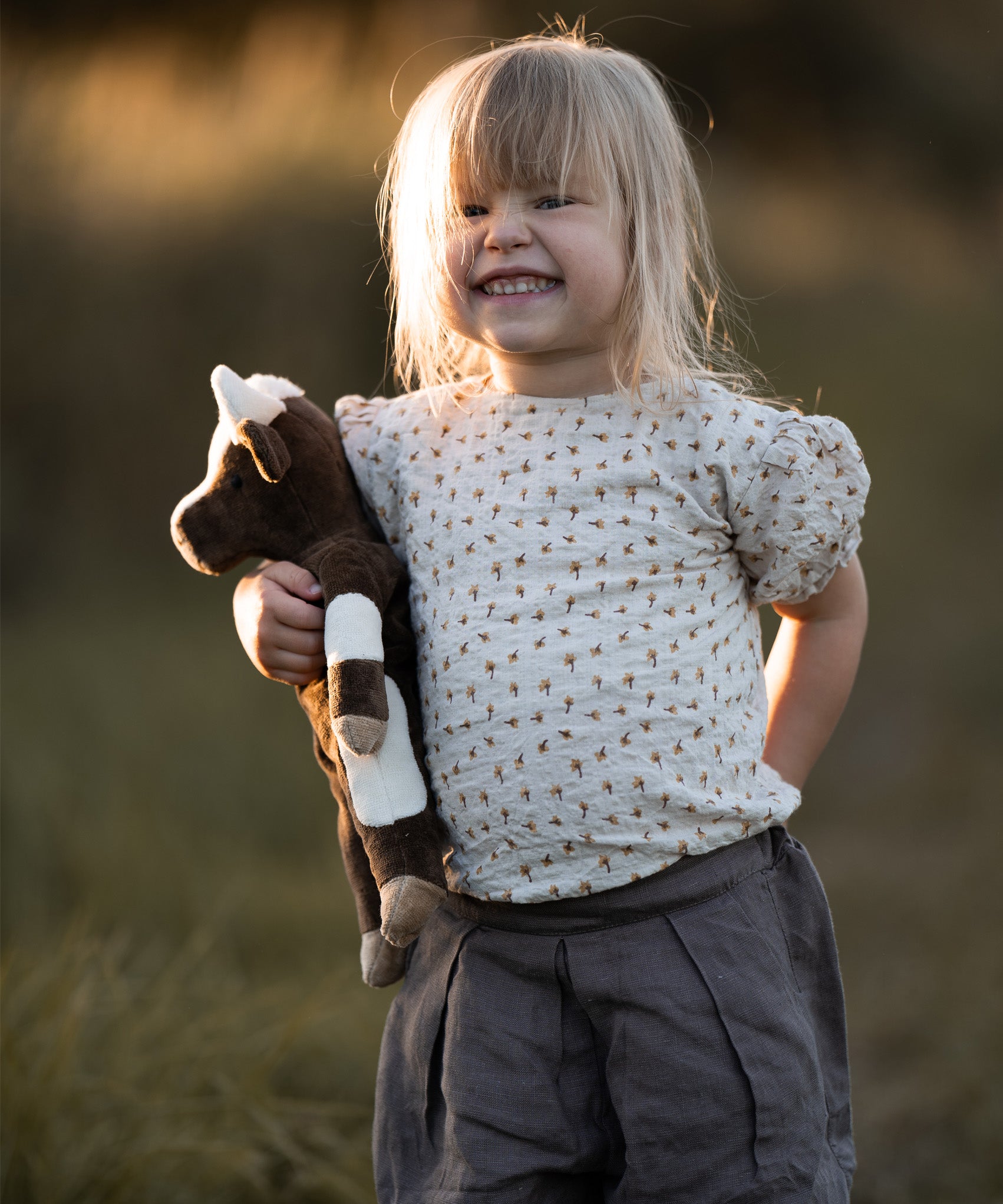 A little girls in a field, holding the Senger organic cotton floppy cow stuffed animal toy. 