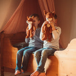 Two children sitting on as wooden bed holding up Senger Floppy Foxes in front of their faces.