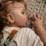 A child laying down next to a Senger organic cotton pink and white check giraffe soft grasping toy, available at Babipur.