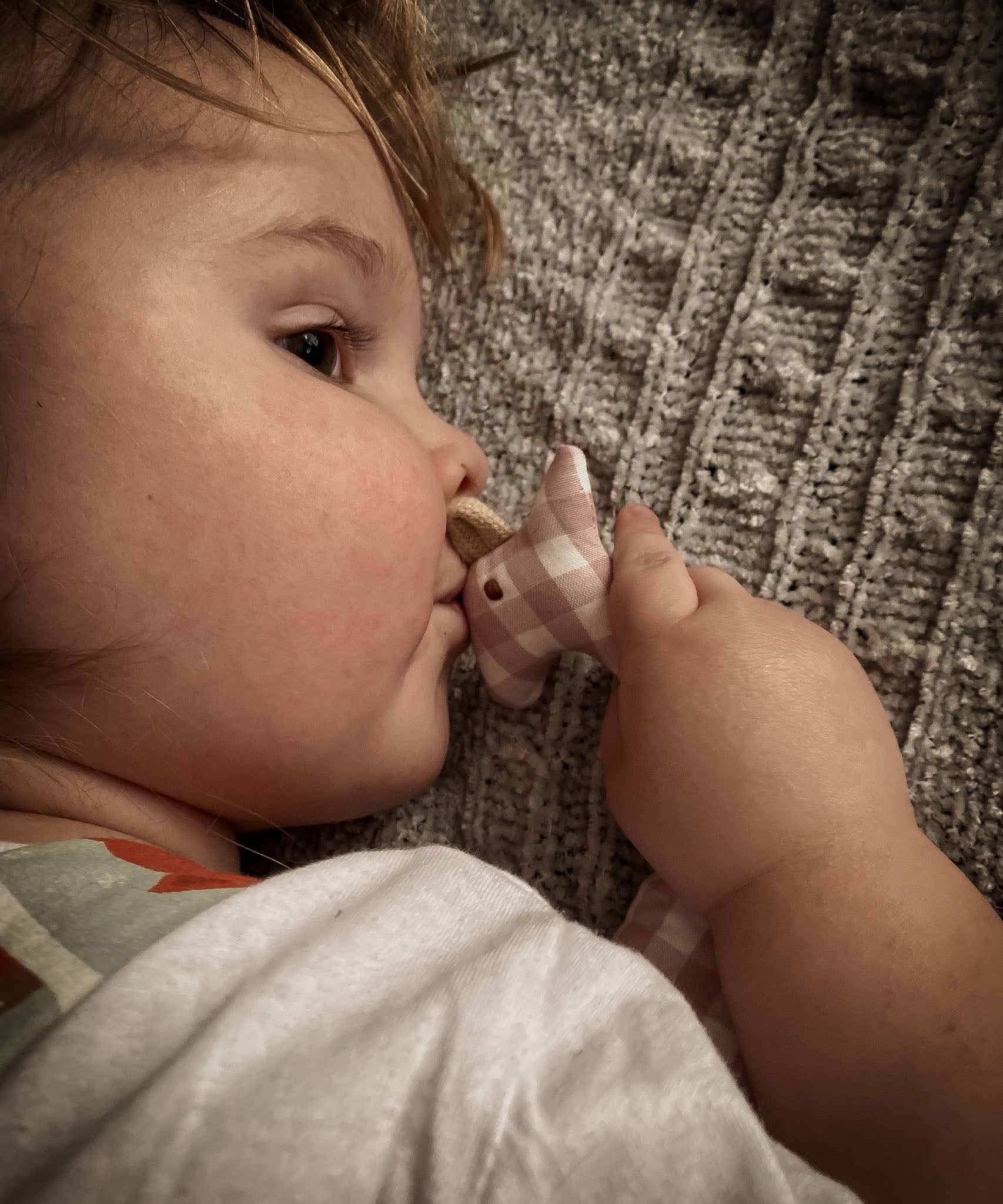 A child giving a Senger organic cotton pink and white check giraffe soft grasping toy a peck on the head. Grasping toy is  available at Babipur.