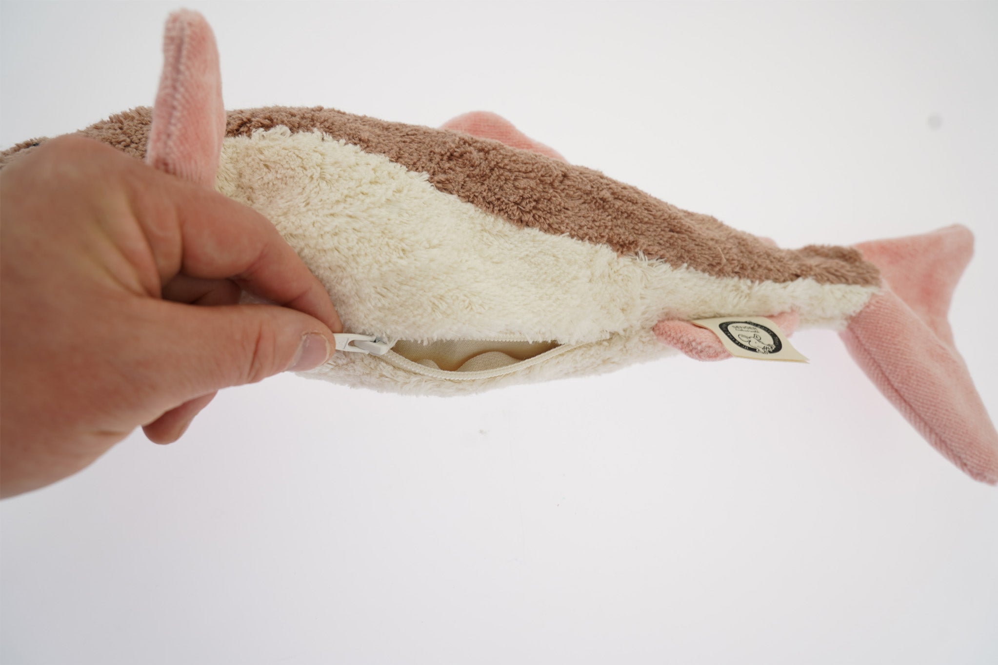 A hand unzipping the belly of the Senger organic cotton cuddly stuffed toy, to take out the heating bag from inside