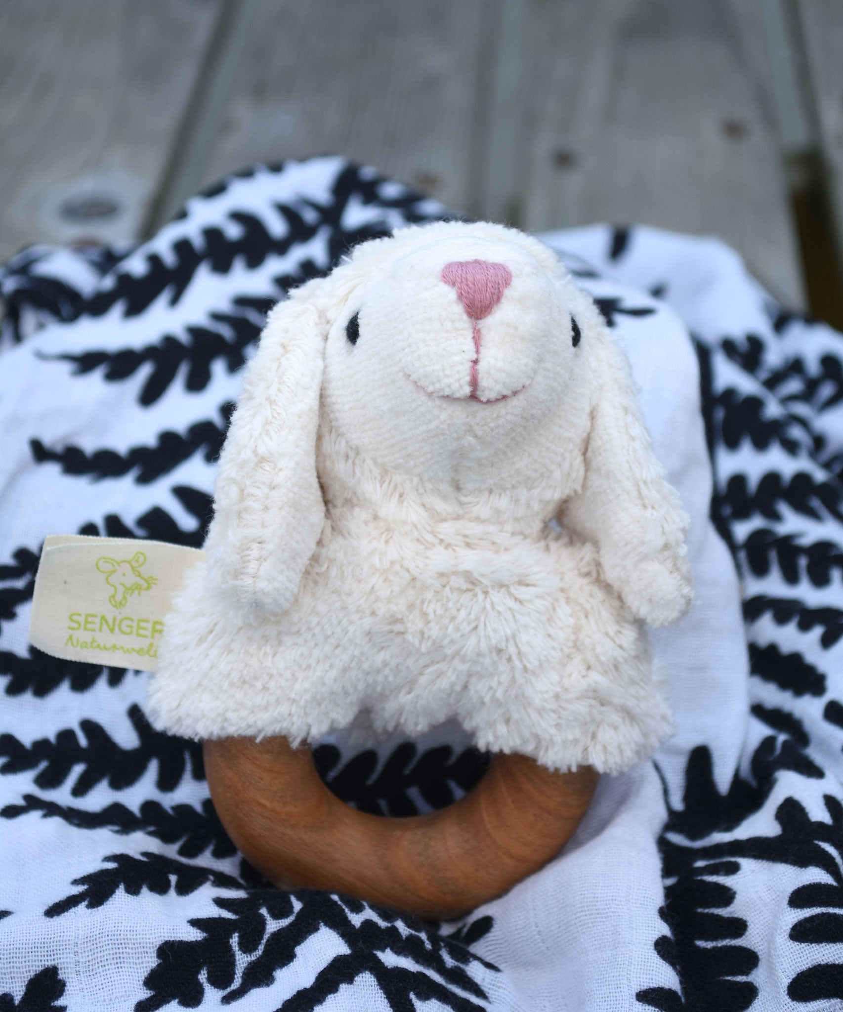 A Senger sheep baby grasping toy placed on a fern print Etta Loves sensory muslin cloth. 