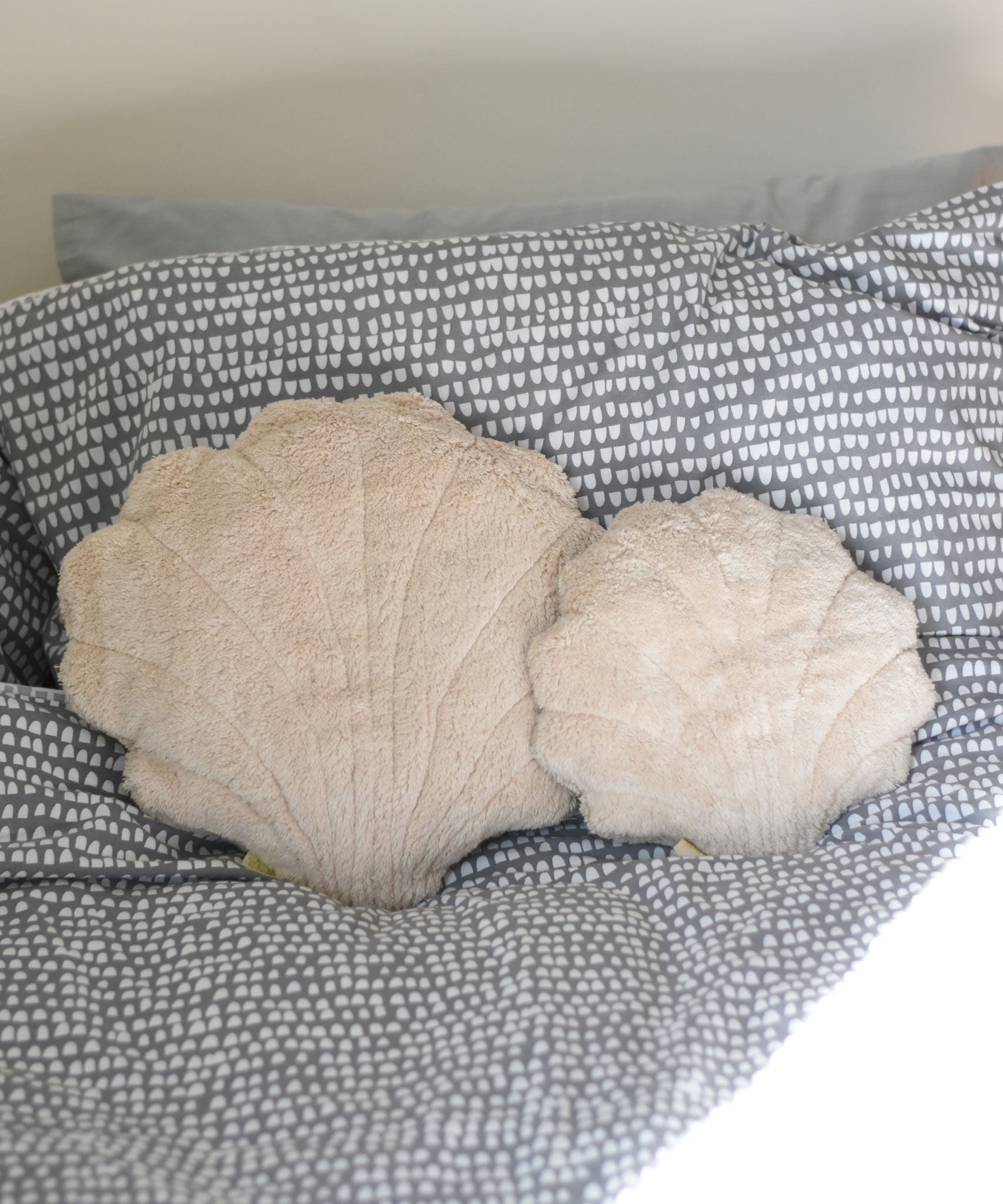A large and small Senger shell cuddly animal soft toy placed on a grey and white coloured bed sheet.