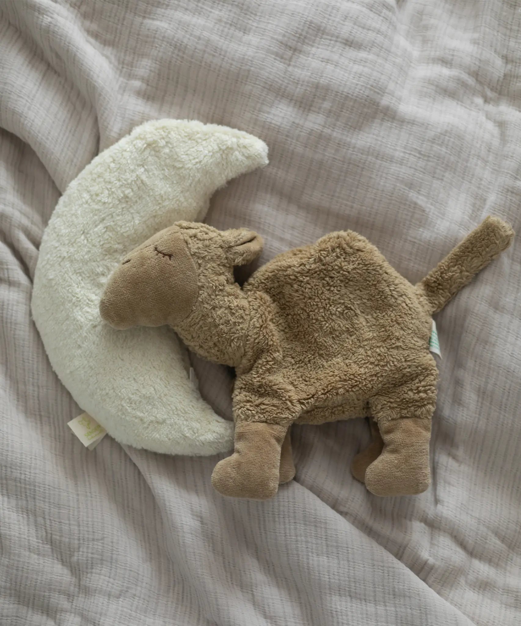 A small Senger brown camel cuddly toy lying flat next to a moon cushion on a blanket