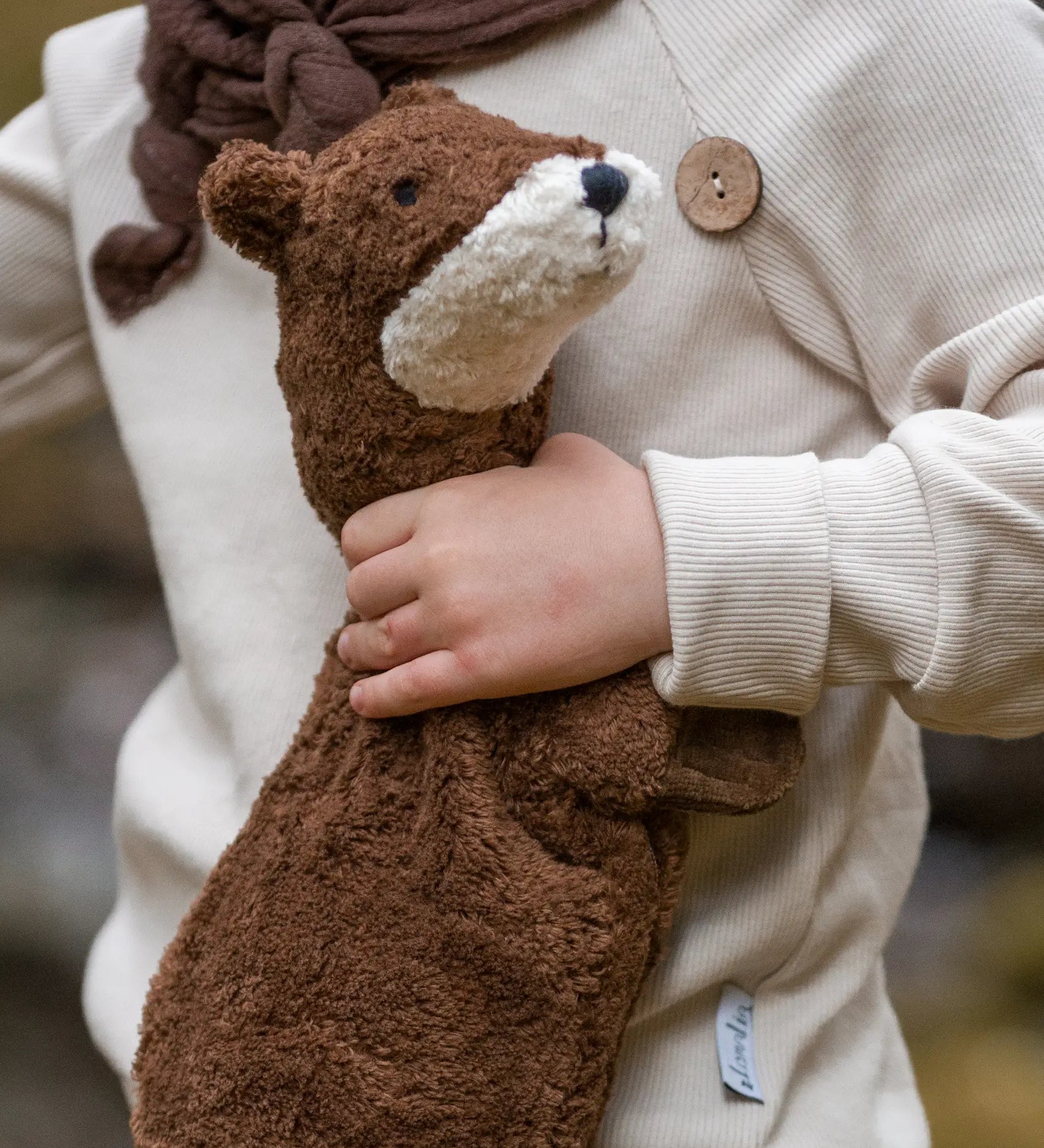 Child holding to a small GOTS organic cotton brown Senger otter cuddly toy
