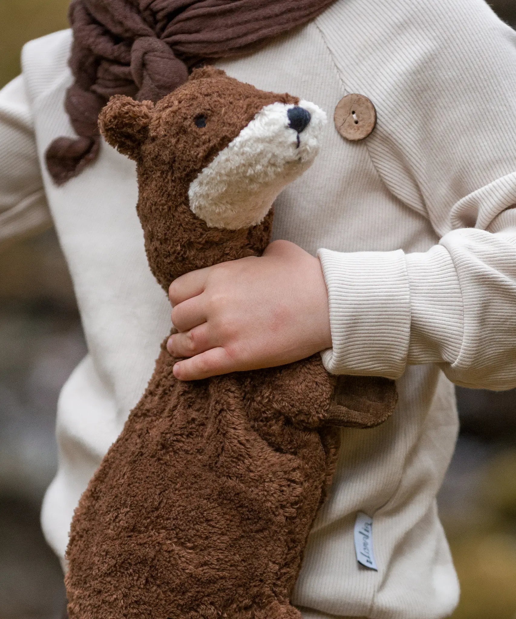 Child holding to a small GOTS organic cotton brown Senger otter cuddly toy