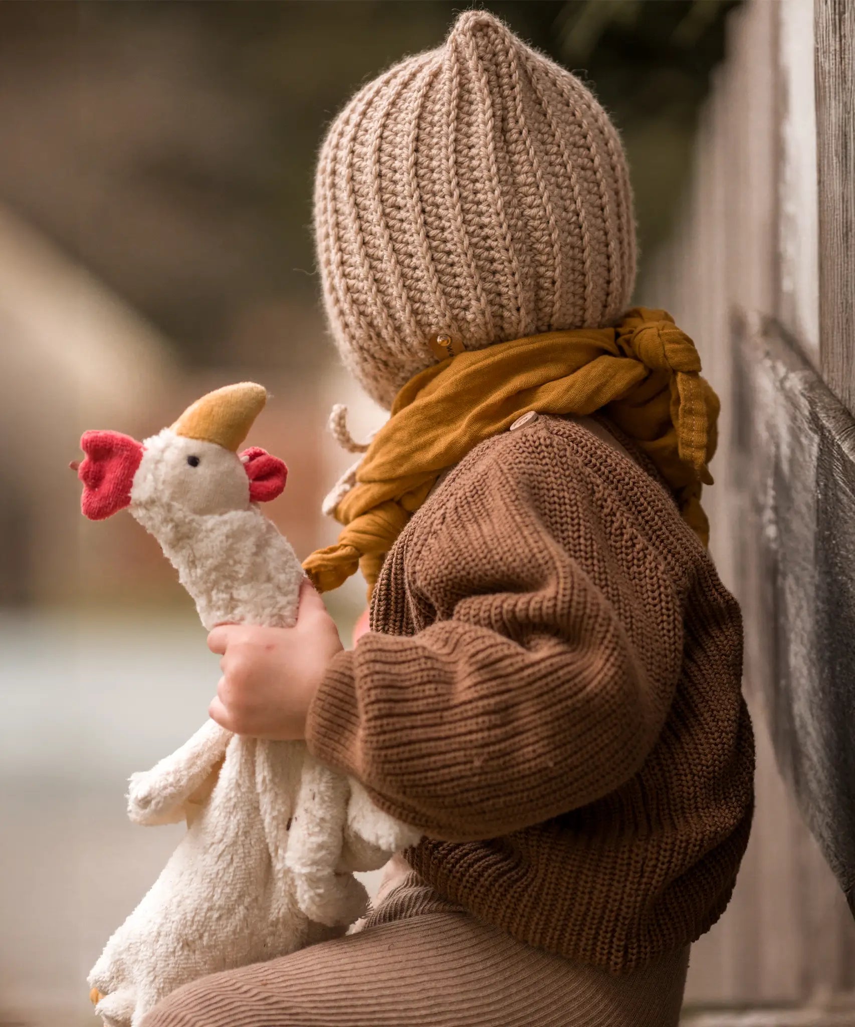 Child holding onto a Senger small cuddly chicken soft toy and sitting on a wooden surface