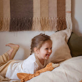 A child laying on a bed with a Senger Small Cuddly Goose organic soft toy in a dark orange Rust colour in front of them. These soft toys are created from the highest quality, sustainable and traceable natural materials. Senger cuddly animal toys and soft dolls are handmade in Germany with love and attention to detail and we are proud Senger stockists here at Babipur. 