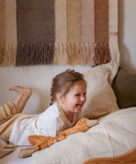 A child laying on a bed with a Senger Small Cuddly Goose organic soft toy in a dark orange Rust colour in front of them. These soft toys are created from the highest quality, sustainable and traceable natural materials. Senger cuddly animal toys and soft dolls are handmade in Germany with love and attention to detail and we are proud Senger stockists here at Babipur. 