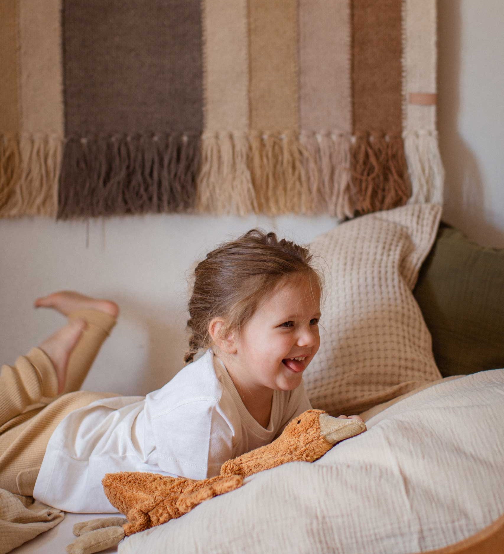 A child laying on a bed with a Senger Small Cuddly Goose organic soft toy in a dark orange Rust colour in front of them. These soft toys are created from the highest quality, sustainable and traceable natural materials. Senger cuddly animal toys and soft dolls are handmade in Germany with love and attention to detail and we are proud Senger stockists here at Babipur. 
