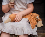 A close up of a Senger Small Cuddly Goose organic soft toy in a dark orange Rust colour on a child's lap. These soft toys are created from the highest quality, sustainable and traceable natural materials. Senger cuddly animal toys and soft dolls are handmade in Germany with love and attention to detail and we are proud Senger stockists here at Babipur. 