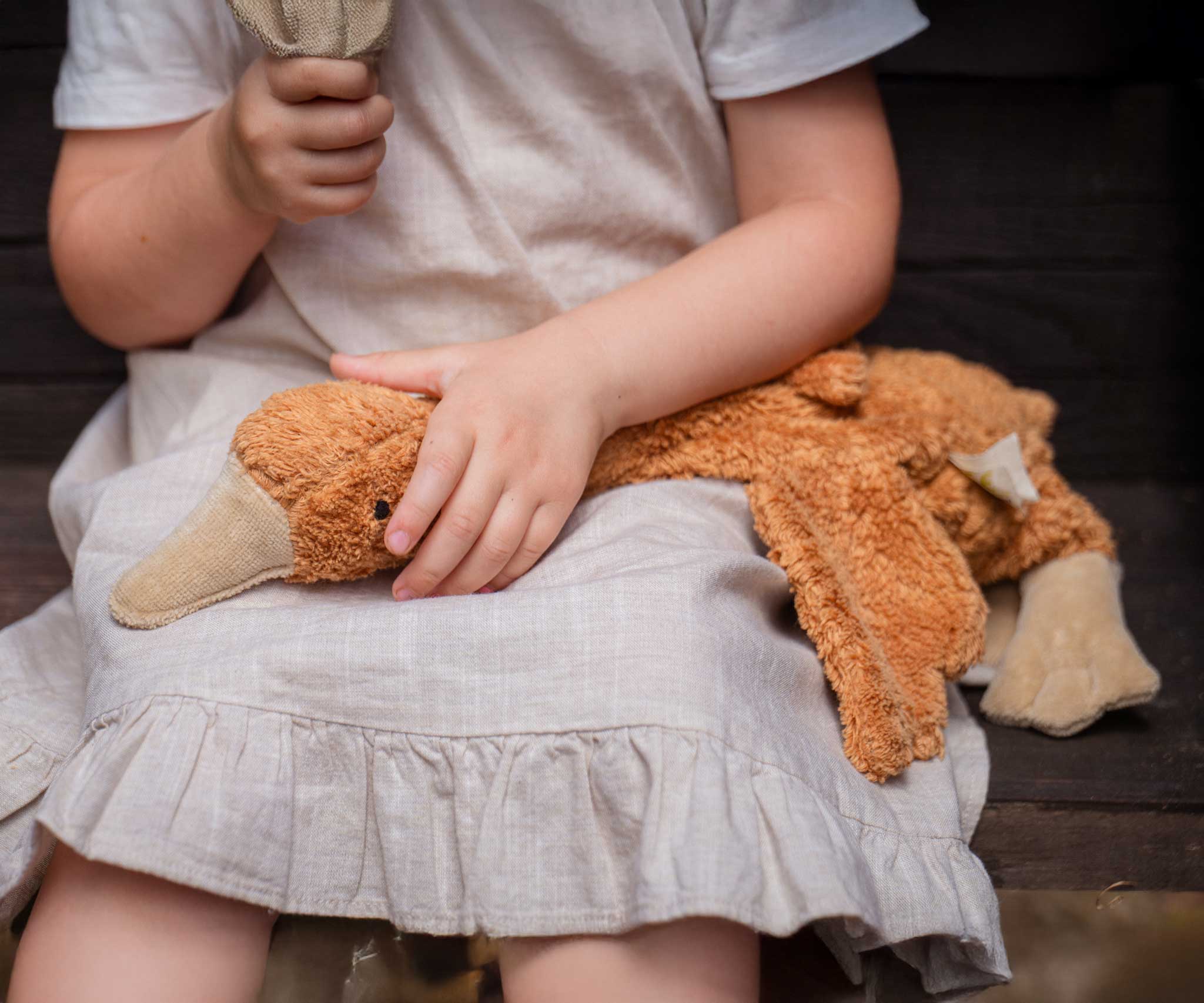 A close up of a Senger Small Cuddly Goose organic soft toy in a dark orange Rust colour on a child's lap. These soft toys are created from the highest quality, sustainable and traceable natural materials. Senger cuddly animal toys and soft dolls are handmade in Germany with love and attention to detail and we are proud Senger stockists here at Babipur. 