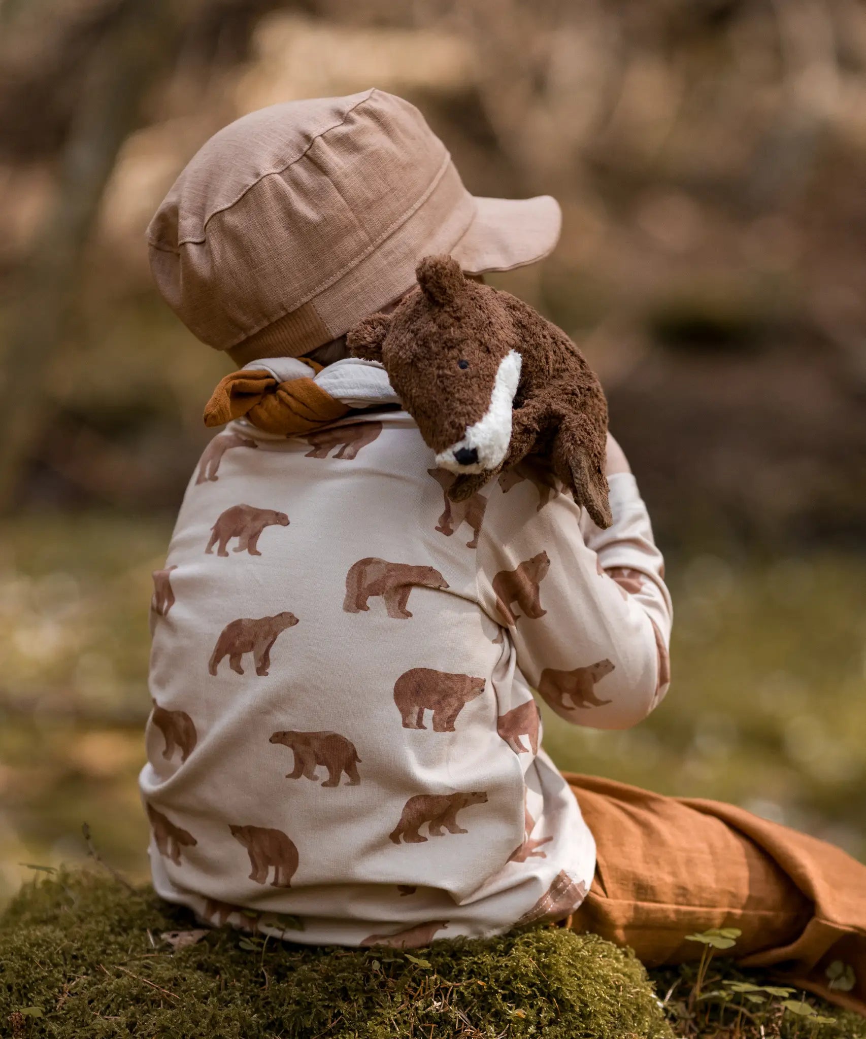 Child with a  small brown Senger otter cuddly toy on their shoulder and sitting on a rock