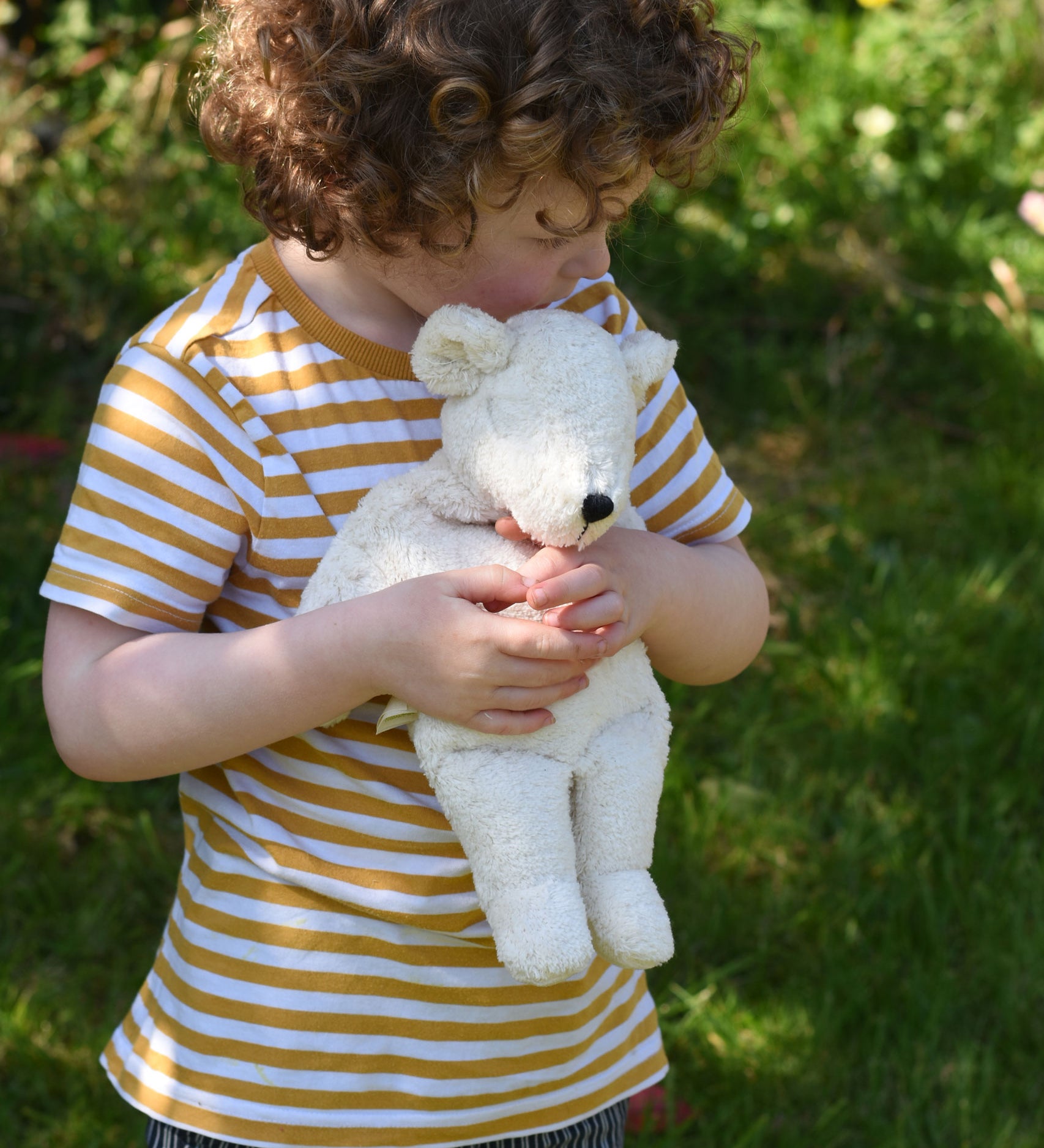 A child cuddling the small Senger polar bear soft toy in their arms.