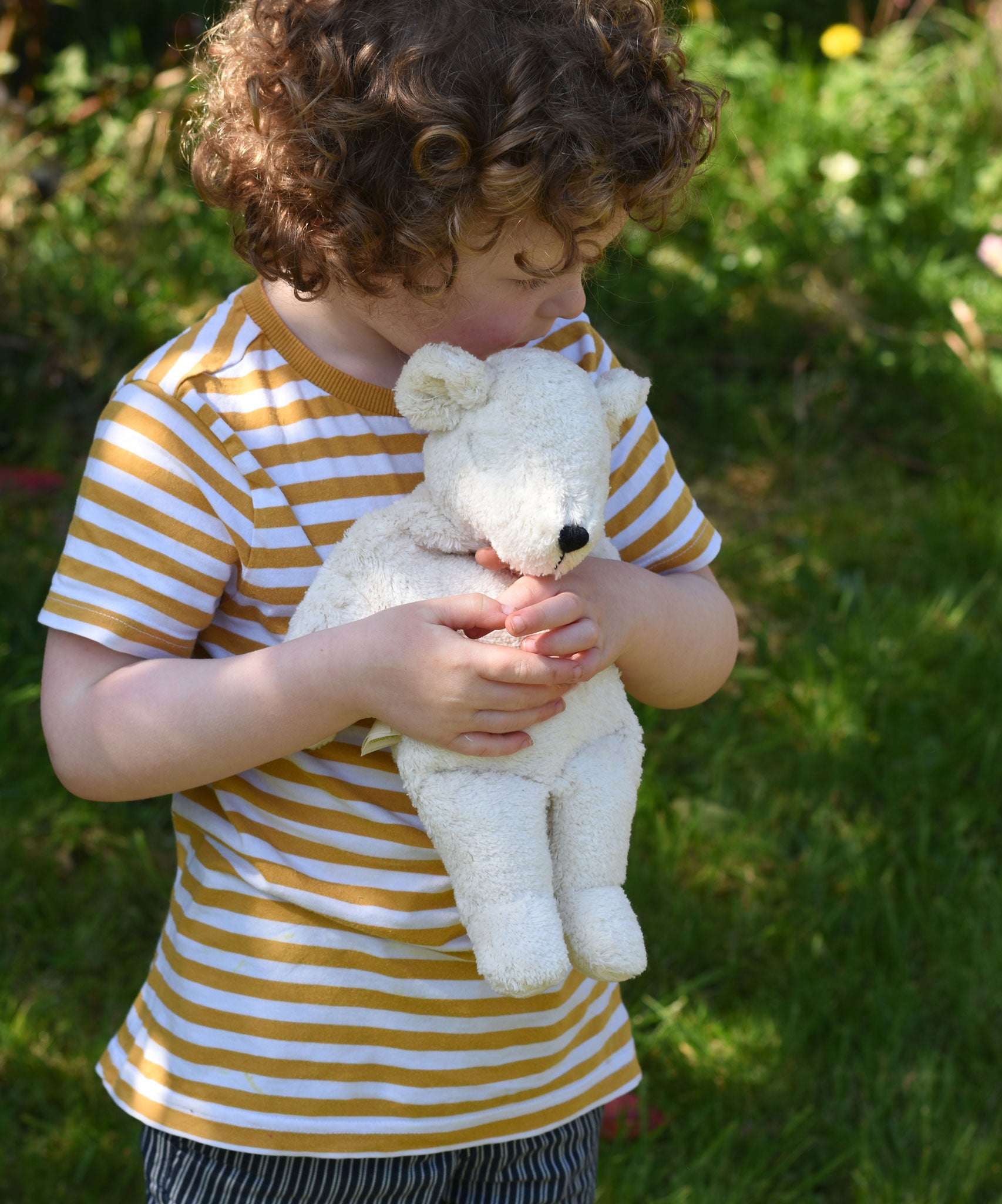 A child cuddling the small Senger polar bear soft toy in their arms.