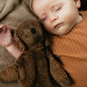 A baby laying next to a Senger Small Cuddly Sheep - Brown.