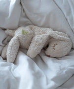 A Senger small cuddly white sheep toy sitting on lying flat on a blanket