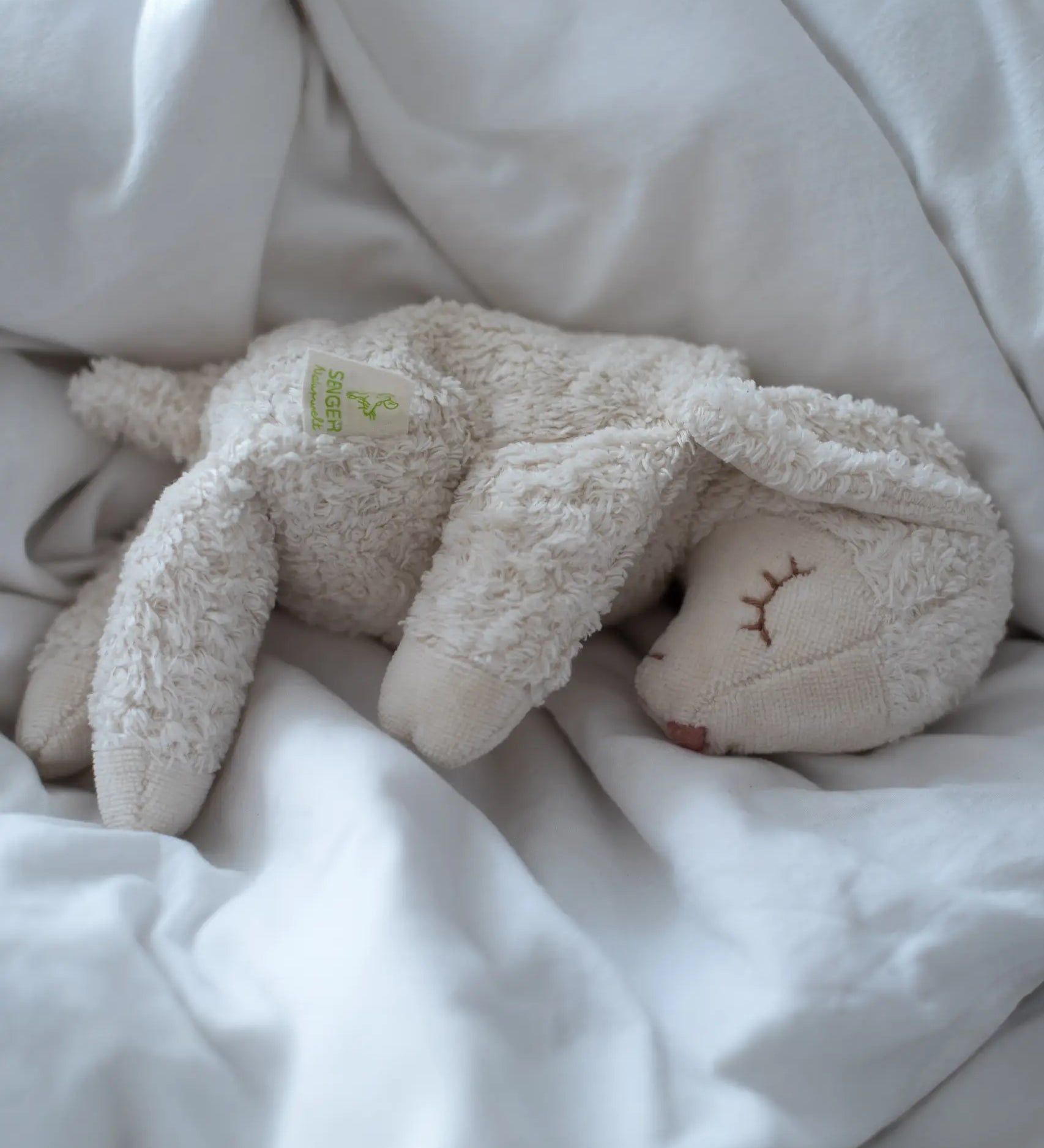 A Senger small cuddly white sheep toy sitting on lying flat on a blanket
