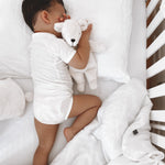 A baby in a cot, cuddling a small Senger white organic cotton teddy bear