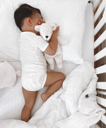 A baby in a cot, cuddling a small Senger white organic cotton teddy bear
