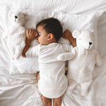A sleeping baby with two Senger organic cotton white teddy bears