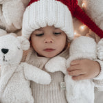 A baby in a Santa hat, cuddling two Senger organic cotton cuddly animal stuffed toys