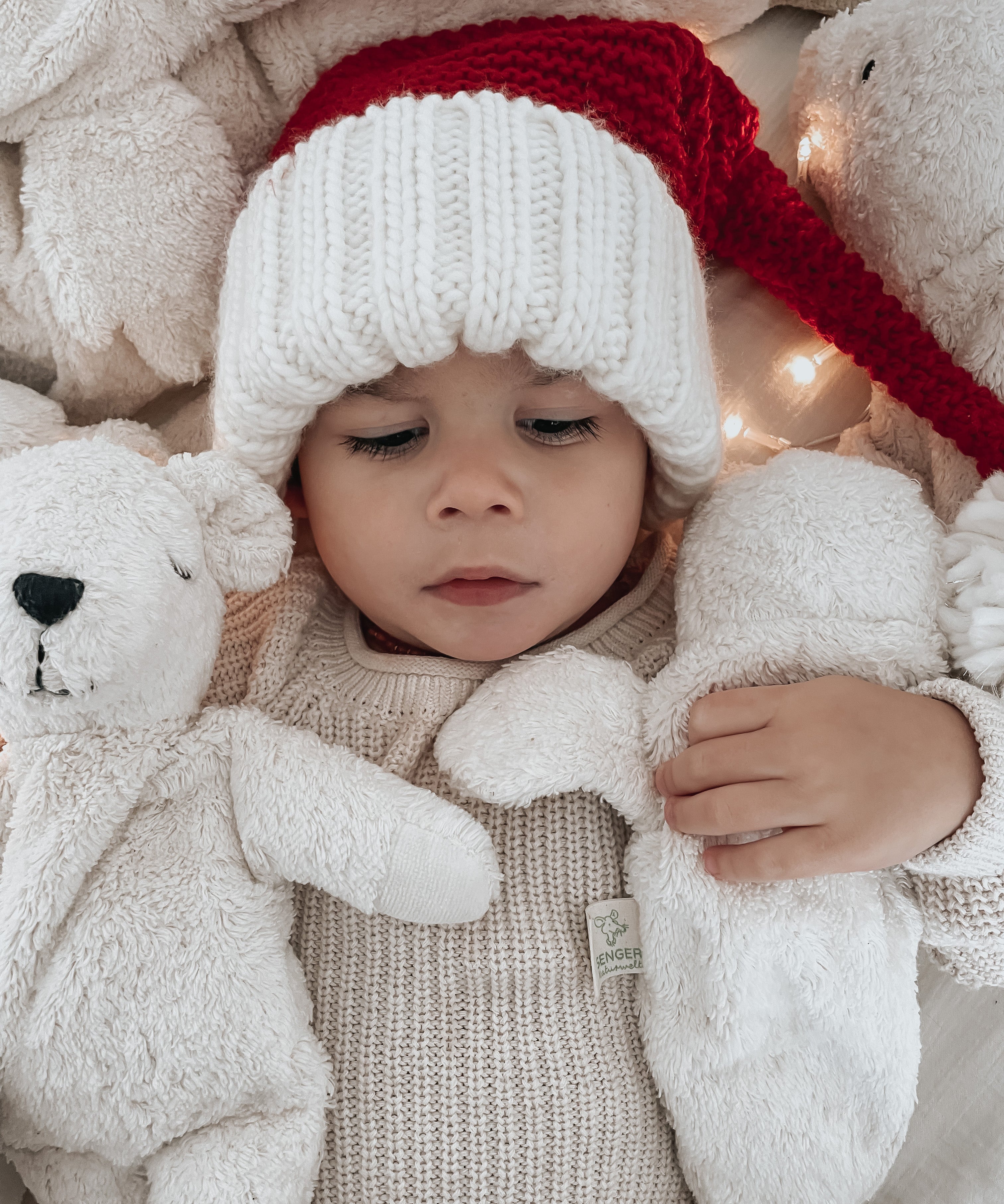 A baby in a Santa hat, cuddling two Senger organic cotton cuddly animal stuffed toys