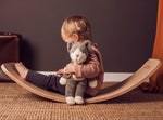 A child sitting on a Wobbel board holding a Senger Small Floppy Cat in one arm.