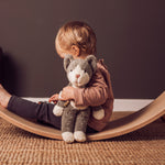 A child sitting on a Wobbel board holding a Senger Small Floppy Cat in one arm.