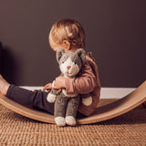 A child sitting on a Wobbel board holding a Senger Small Floppy Cat in one arm.