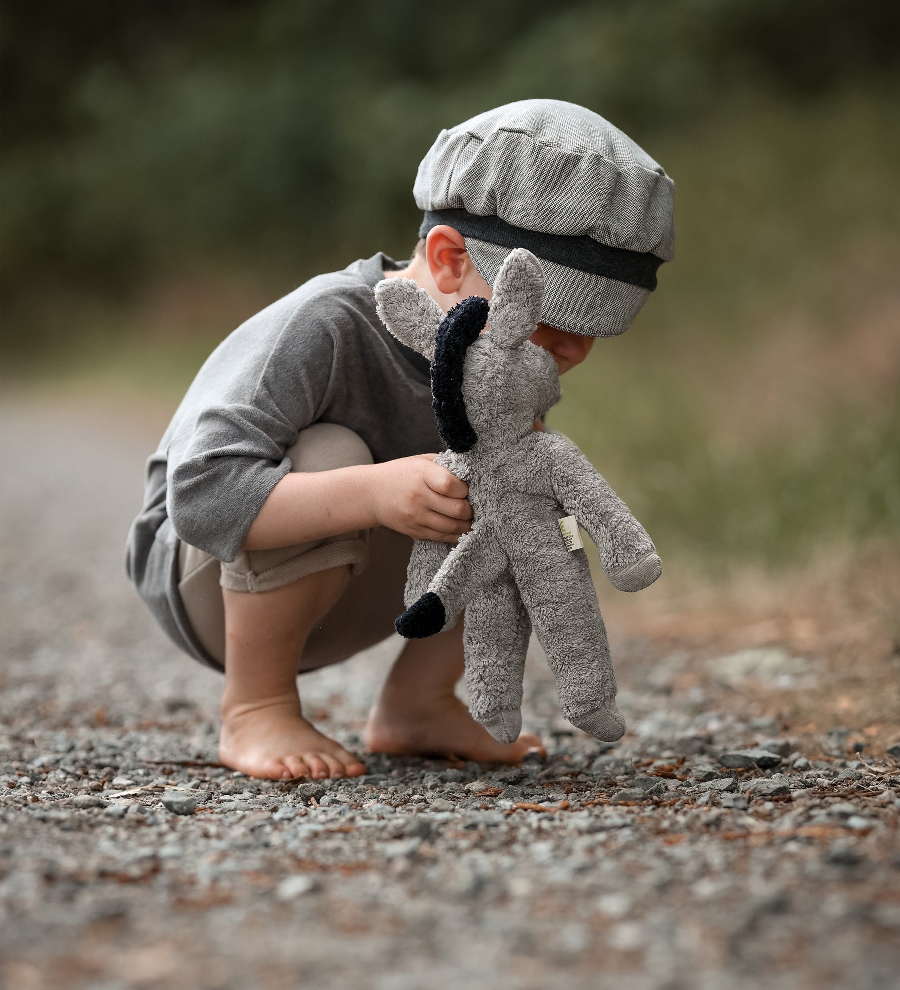 A small child bent down, playing with the Senger organic cotton stuffed floppy donkey toy. 