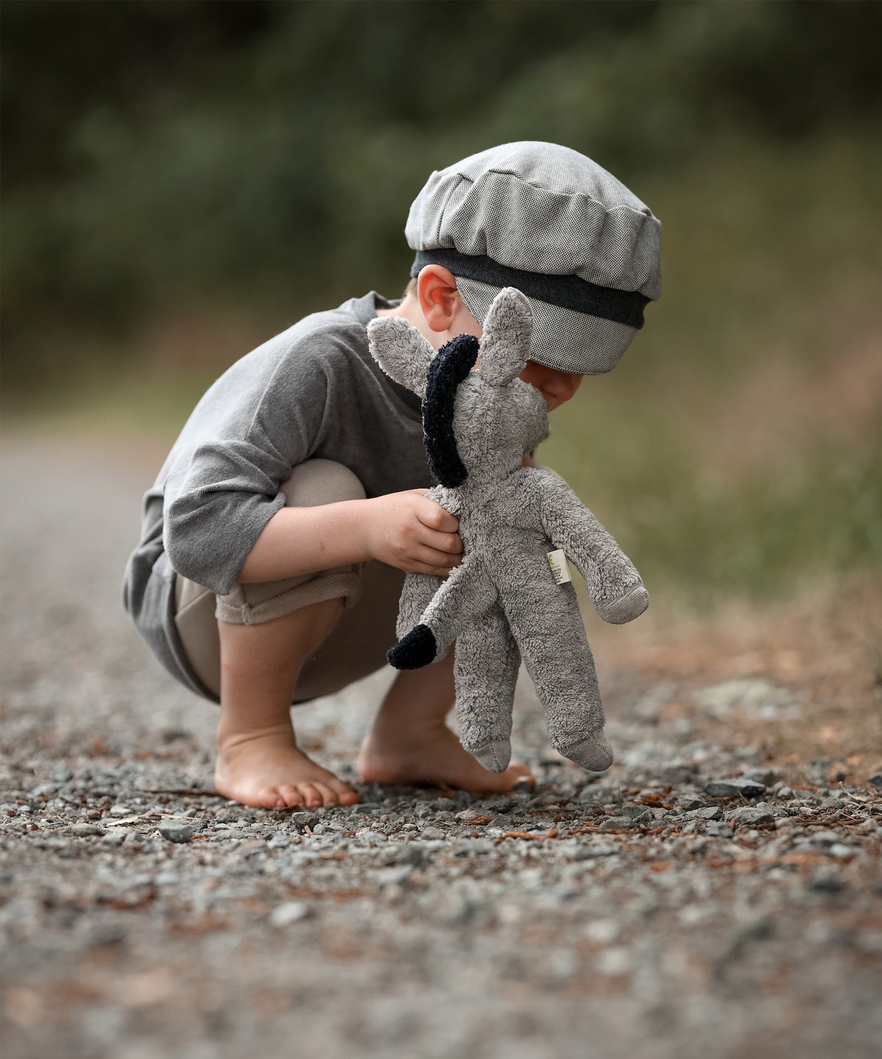 A small child bent down, playing with the Senger organic cotton stuffed floppy donkey toy. 