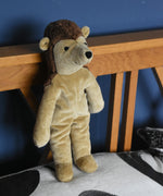 A Senger small floppy hedgehog soft toy placed in a standing position against a wooden headboard on a pillow. This hedgehog is part of a wider selection of soft toys made with organic cotton and natural fillings that are available at Babipur. 