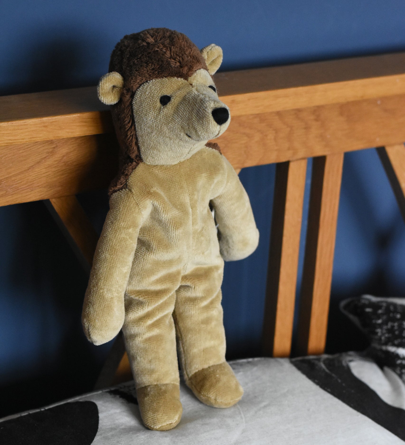 A Senger small floppy hedgehog soft toy placed in a standing position against a wooden headboard on a pillow. This hedgehog is part of a wider selection of soft toys made with organic cotton and natural fillings that are available at Babipur. 