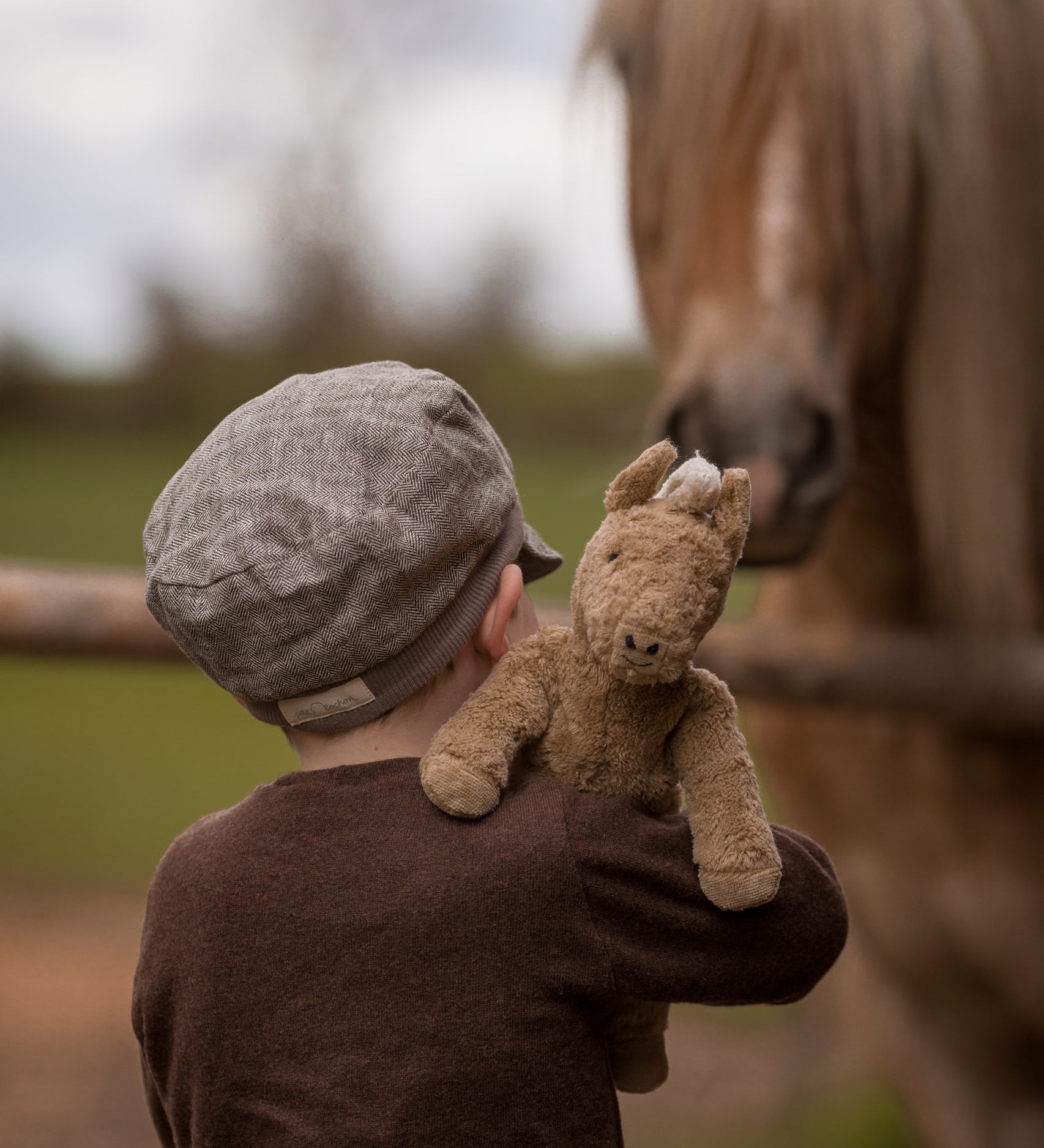 A child holding up  Senger Small Floppy Horse on their shoulder.